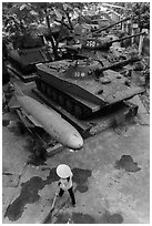 Woman sweeping floor in front of military hardware, military museum. Hanoi, Vietnam (black and white)