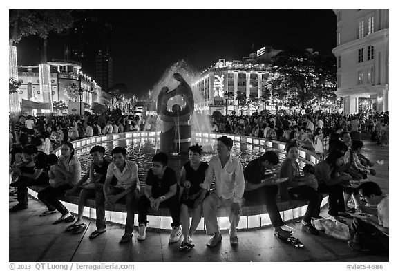 People sitting on fountain at night, New Year eve. Ho Chi Minh City, Vietnam (black and white)