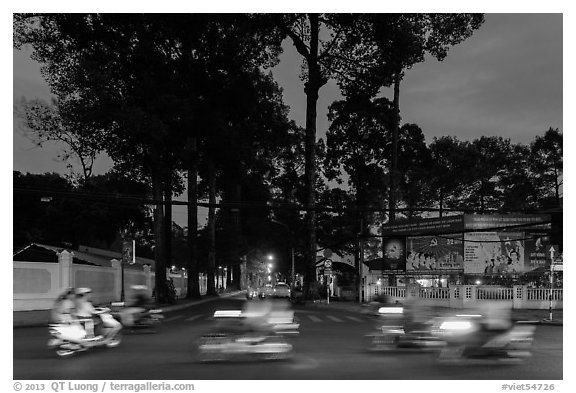 Blurred motorbikes at dusk and tall trees next to Van Hoa Park. Ho Chi Minh City, Vietnam (black and white)