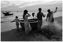 Fishermen folding net out of coracle boat as children watch. Mui Ne, Vietnam ( black and white)