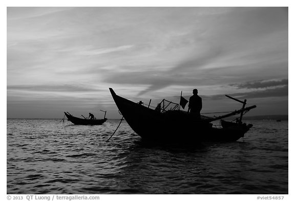 Men on fishing skiffs under bright sunset skies. Mui Ne, Vietnam