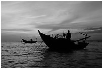 Men on fishing skiffs under bright sunset skies. Mui Ne, Vietnam (black and white)