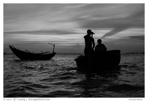 Men silhouetted paddling coracle boat at sunset. Mui Ne, Vietnam