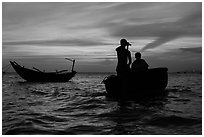 Men silhouetted paddling coracle boat at sunset. Mui Ne, Vietnam ( black and white)