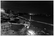 Man with fire next to coracle boat at night. Mui Ne, Vietnam (black and white)