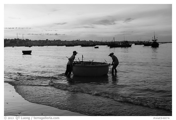 Fishermen pushing coracle boat at dawn. Mui Ne, Vietnam