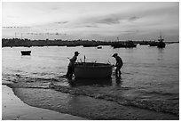 Fishermen pushing coracle boat at dawn. Mui Ne, Vietnam (black and white)