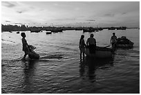 Fishermen using coracle boats to transport cargo at dawn. Mui Ne, Vietnam (black and white)