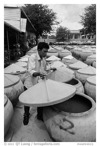 Man lifting covers of jars with fermented fish sauce. Mui Ne, Vietnam