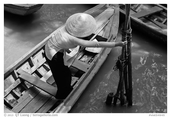 Woman in ao dai reaching to bamboo poles from boat. My Tho, Vietnam (black and white)