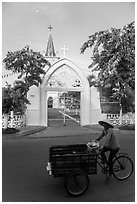 Woman bicycling in front of church. Tra Vinh, Vietnam (black and white)