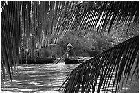 Woman paddling boat on river channel, framed by leaves. Can Tho, Vietnam ( black and white)