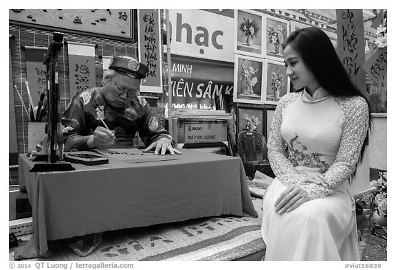 Caligrapher draws lunar new year greetings for beautiful woman in ao ai. Ho Chi Minh City, Vietnam (black and white)