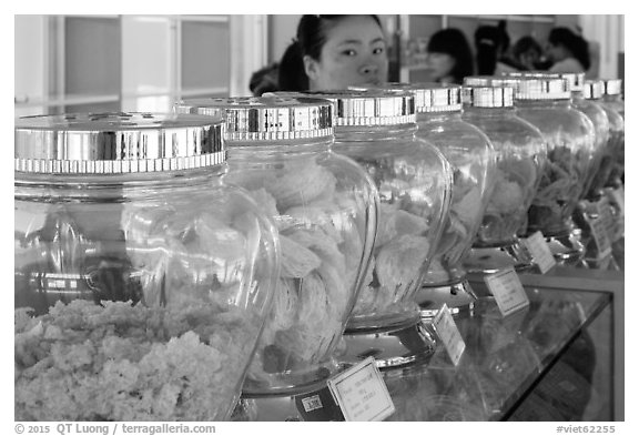 Woman peering over row of eddible birds nest jars. Con Dao Islands, Vietnam (black and white)