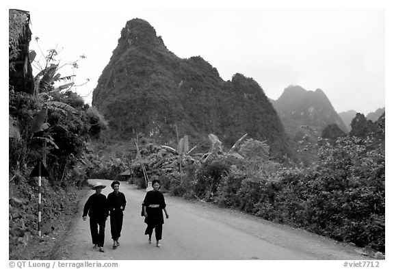 Villagers in traditional garb walking down the road with limestone peaks in the background, Ma Phuoc Pass area. Northeast Vietnam (black and white)