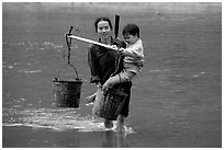 Tay Woman carrying child and water buckets across river. Northeast Vietnam (black and white)