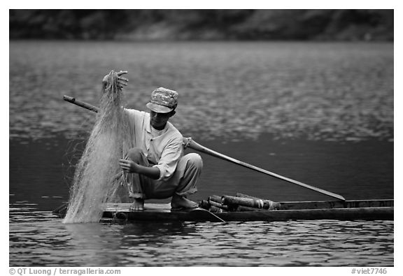 Fisherman retrieves net from a dugout boat. Northeast Vietnam (black and white)