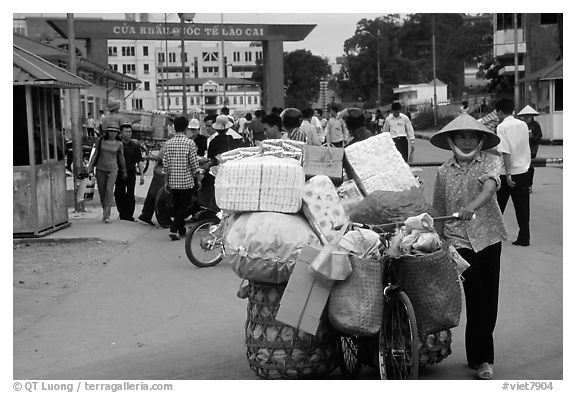 Woman pushing a bicycle loaded with cheap goods at the Lao Cai border crossing. Vietnam (black and white)