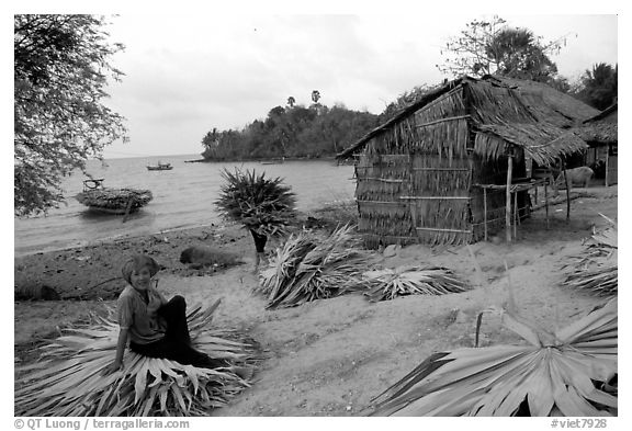 Woman taking a break sitting on leaves used to build a hut. Hong Chong Peninsula, Vietnam