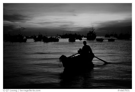 Man in a small boat, with moored boats seen against a vivid sunset. Vung Tau, Vietnam