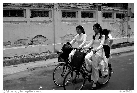 Senior high school girls ride bicycles with impeccable style, wearing elegant Ao Dai uniforms. Ho Chi Minh City, Vietnam (black and white)