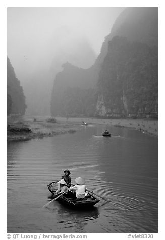 Villagers going by boat to their fields, amongst misty cliffs, Tam Coc. Ninh Binh,  Vietnam (black and white)