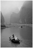 Villagers going by boat to their fields, amongst misty cliffs, Tam Coc. Ninh Binh,  Vietnam (black and white)