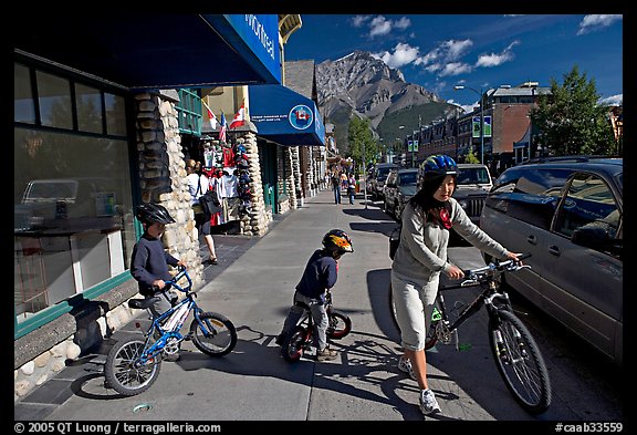 Woman and kids with mountain bikes on downtown Banff sidewalk. Banff National Park, Canadian Rockies, Alberta, Canada (color)