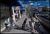 Woman and kids with mountain bikes on downtown Banff sidewalk. Banff National Park, Canadian Rockies, Alberta, Canada