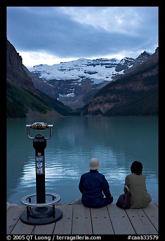 Couple sitting at the edge of Lake Louise at dawn. Banff National Park, Canadian Rockies, Alberta, Canada (color)