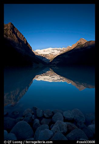 Boulders, Mirror-like Lake Louise and Victoria Peak, early morning. Banff National Park, Canadian Rockies, Alberta, Canada (color)