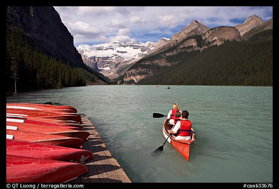 Canoeists paddling out of the boat dock in blue-green waters, Lake Louise, morning. Banff National Park, Canadian Rockies, Alberta, Canada