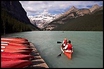 Canoeists paddling out of the boat dock in blue-green waters, Lake Louise, morning. Banff National Park, Canadian Rockies, Alberta, Canada