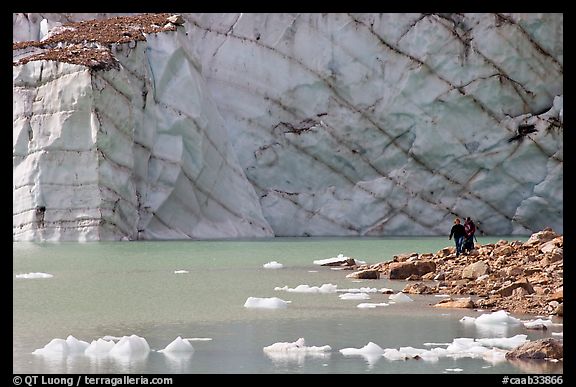 Hikers on the shore of Cavell Pond with high glacier wall behind. Jasper National Park, Canadian Rockies, Alberta, Canada (color)