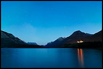 Waterton lake by night with stars in the sky in lights of Price of Wales Hotel. Waterton Lakes National Park, Alberta, Canada