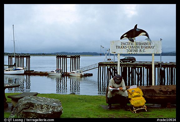 Backpacker sitting under the Transcanadian terminus sign, Tofino. Vancouver Island, British Columbia, Canada (color)