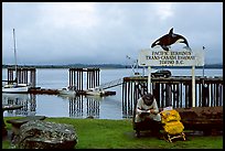 Backpacker sitting under the Transcanadian terminus sign, Tofino. Vancouver Island, British Columbia, Canada (color)