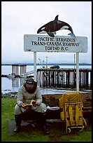 Backpacker sitting under the Transcanadian terminus sign, Tofino. Vancouver Island, British Columbia, Canada (color)