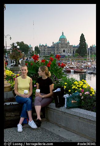 Women with shopping bags and coffee cups at the Inner Harbour, sunset. Victoria, British Columbia, Canada