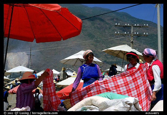 Bai women examining a piece of cloth at the Monday market. Shaping, Yunnan, China (color)