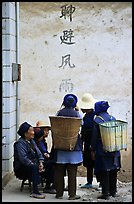 Elderly women with back baskets in front of a wall with Chinese scripture. Shaping, Yunnan, China (color)