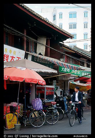 Man on bicycle in front of wooden buildings. Kunming, Yunnan, China