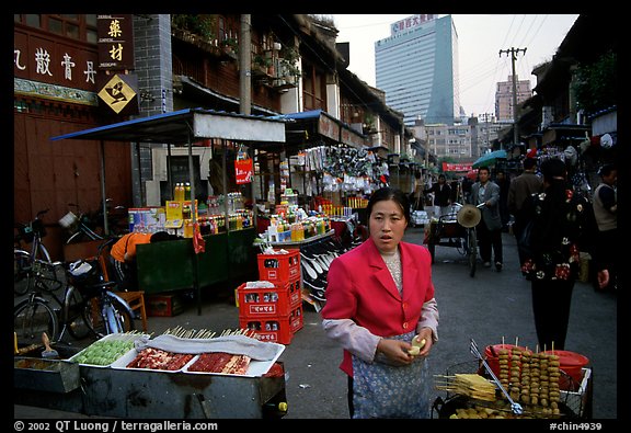 Street market in an old alley of wooden buildings, with a high rise in the background. Kunming, Yunnan, China (color)