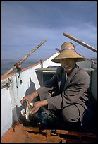 Cormorant fisherman recovers a fish from the throat of one of his birds. Dali, Yunnan, China (color)