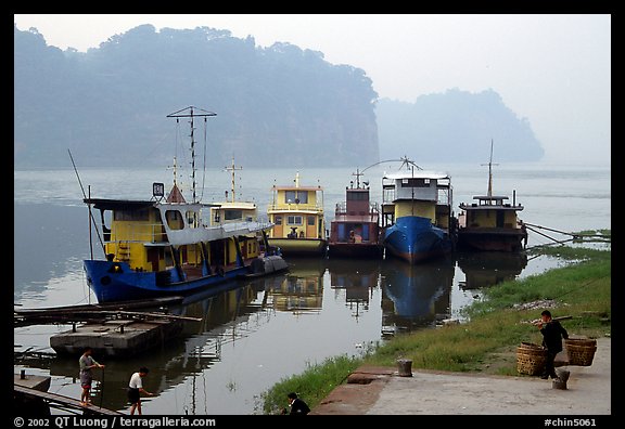 Boats along the river with misty cliffs in the background. Leshan, Sichuan, China