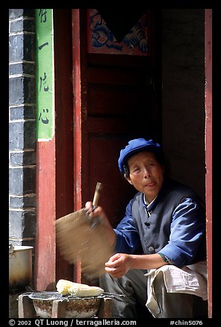 Naxi woman at doorway selling broiled corn. Lijiang, Yunnan, China (color)