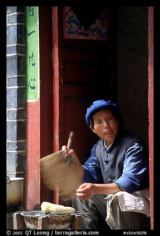 Naxi woman at doorway selling broiled corn. Lijiang, Yunnan, China