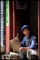 Naxi woman at doorway selling broiled corn. Lijiang, Yunnan, China