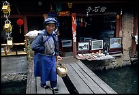 Naxi woman peddling eggs  to local residents walks acros a canal. Lijiang, Yunnan, China