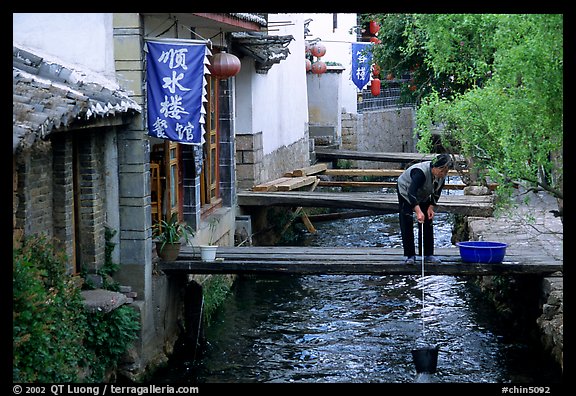 Woman fills up a water buck in the canal. Lijiang, Yunnan, China (color)